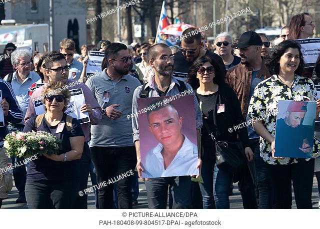 08 April 2018, Germany, Berlin: People walking through Britz holding photos of Burak.B on their way to the unveiling of a memorial