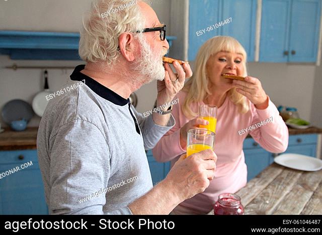 Aged married couple having meal in morning. Elderly grayhaired man enjoying some jelly toasts and orange juice with his wife for breakfast in their house
