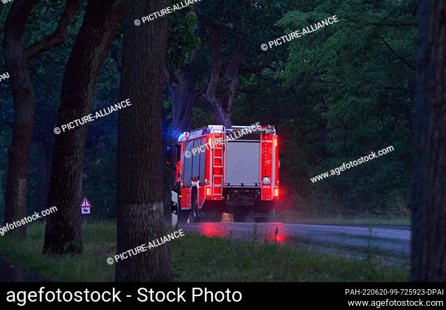 20 June 2022, Brandenburg, Treuenbrietzen: It's raining while a fire truck is driving with blue lights in the early morning hours in the forest area between...