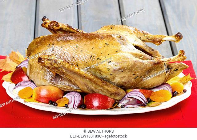 Roasted goose with apples and vegetables on wooden table