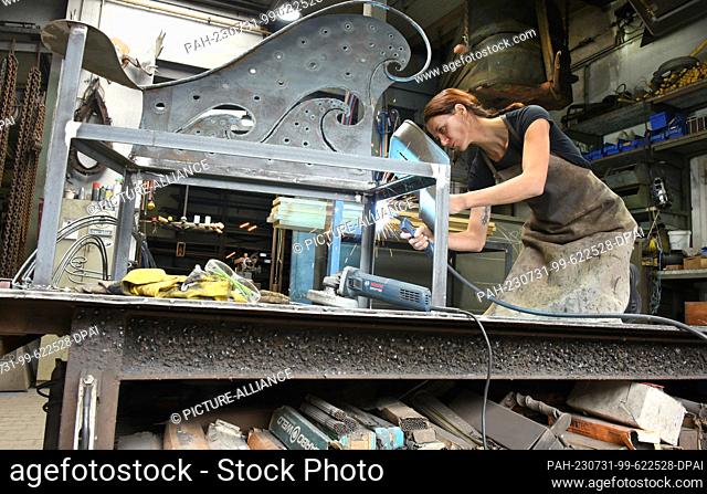 27 July 2023, Saxony, Hohenprießnitz: Blacksmith and metal designer Marika Widdermann works on a two-seater bench in her father Roger Widdermann's forge