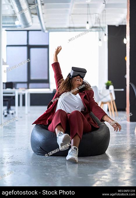 Cheerful female professional using wearable computer on bean bag at coworking office