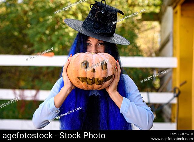 A girl in a witch costume looks out from behind a pumpkin with a painted face