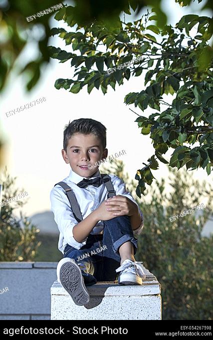 Adorable little boy wearing stylish outfit posing confidently at camera sitting on fence