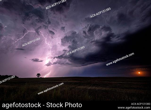 A rising moon and a storm with lightning striking over field in rural North Dakota United States