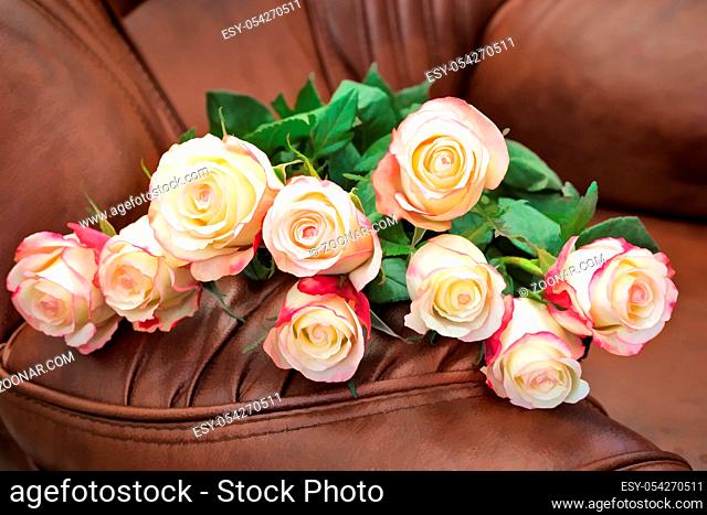 Still life : on the leather brown chair lay a bouquet of beautiful roses