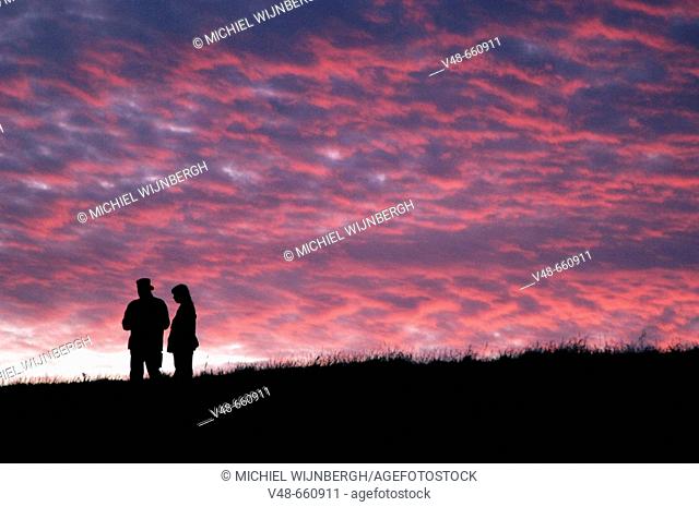 Sunset with silhouettes of two persons on the top of a dike. Netherlands (August, 2005)