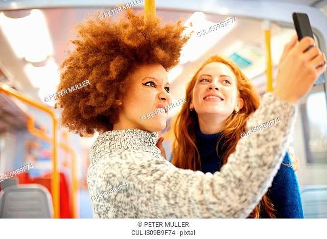 Friends taking selfie with mobile phone on train, London