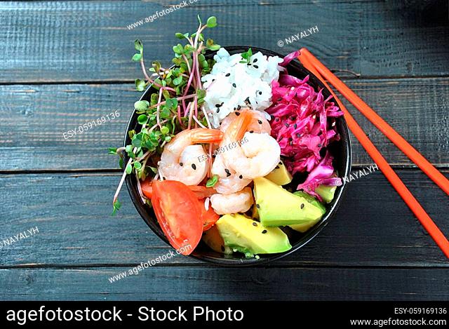 Organic food. Fresh seafood recipe. Poke bowl with shrimps, rice, fresh red cabbage, avocado, cherry tomatoes, radish sprouts on wooden background