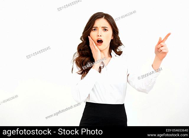 Business Concept: Portrait of surprised young businesswoman pointing finger away to copy space. Isolated on a white background