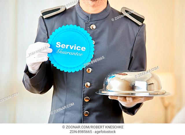 Page hält Service Garantie Schild und Speiseglocke als Symbol der Qualität