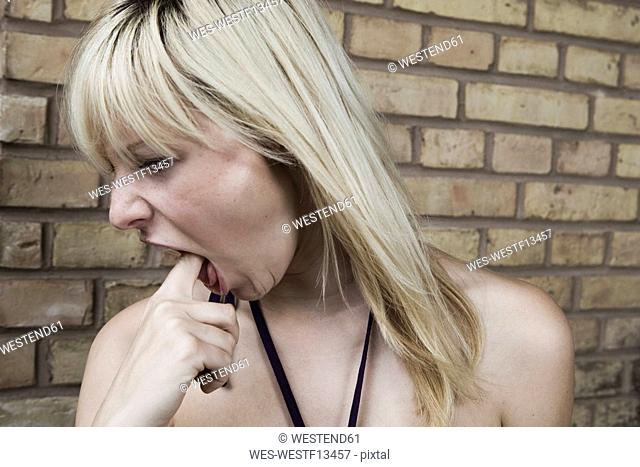Germany, Berlin Young woman with finger in mouth, portrait, close-up