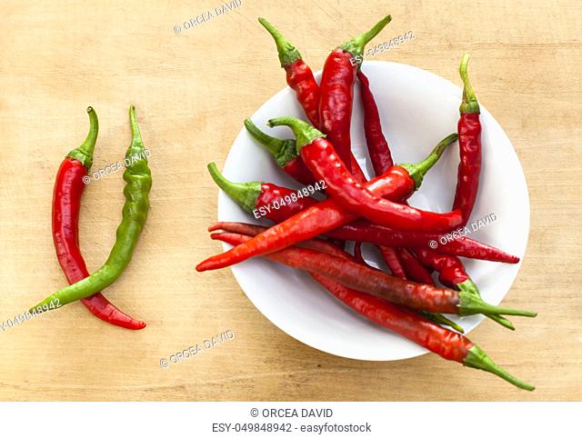 Red chili with one green cilli pepper in a bowl on wood background