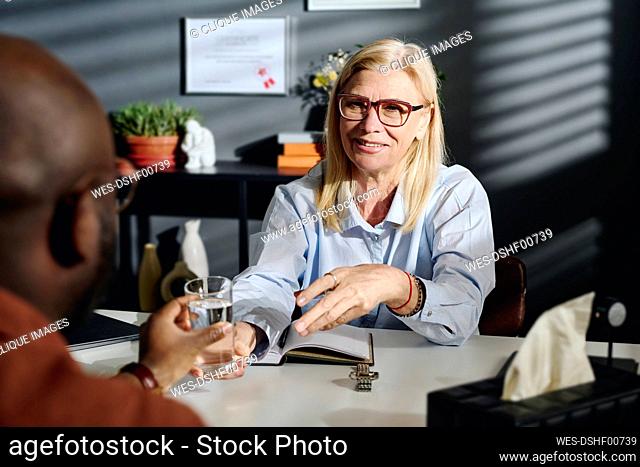 Smiling blond psychologist giving glass of water to patient at office