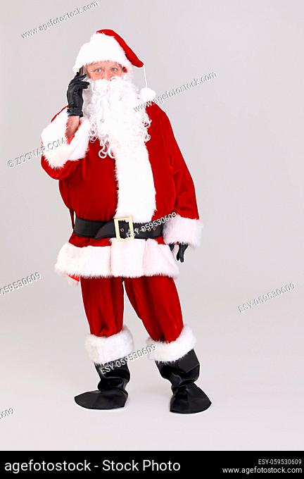 Full size portrait of Santa talking on mobile phone, looking at camera, isolated on gray background