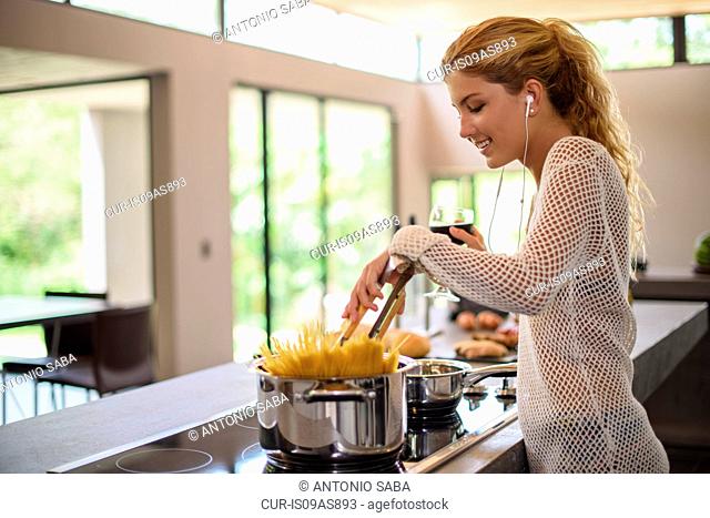 Young woman cooking spaghetti in kitchen