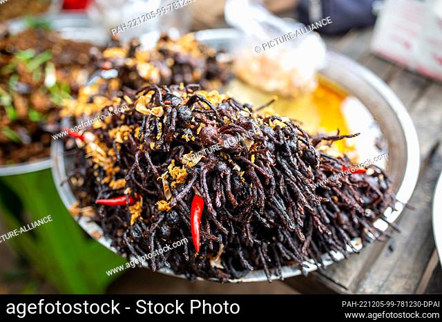PRODUCTION - 19 November 2022, Cambodia, Udong: Many fried tarantulas with crispy garlic and fresh chili peppers are piled up on a plate l at the Udong market