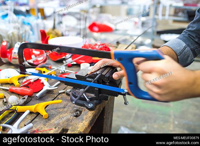 Man working with saw on fencing weapon on workbench