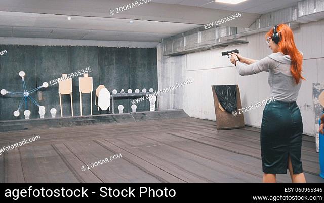 Woman with red hair shooting with a gun in shooting gallery, horizontal