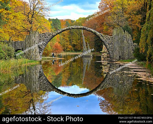 07 November 2023, Saxony, Kromlau: The Rakotzbrücke bridge in the autumnal azalea and rhododendron park in Kromlau in the district of Görlitz near the state...