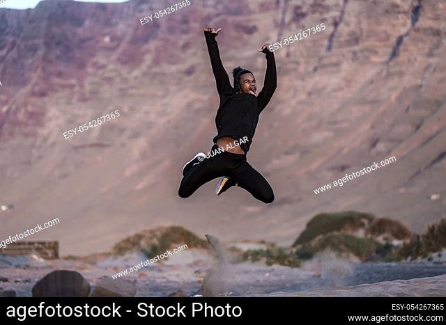 Young African American guy leaping up and screaming in excitement while spending time in amazing nature