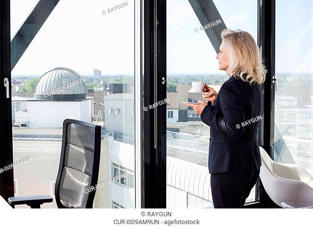 Businesswoman drinking coffee by window