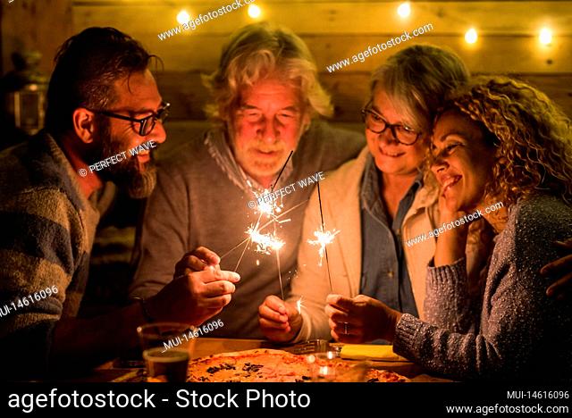 group of people celebrating the 2021 new year after a hard 2020 - bye 2020 concept - family enjoying and having fun together with sparklers at home eating pizza...
