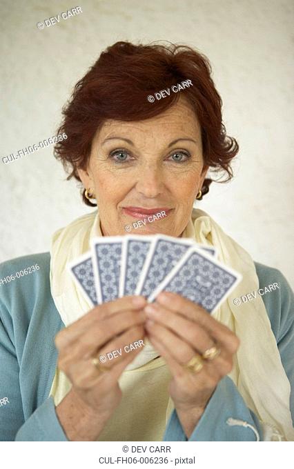 Senior woman holding playing cards, smiling, portrait