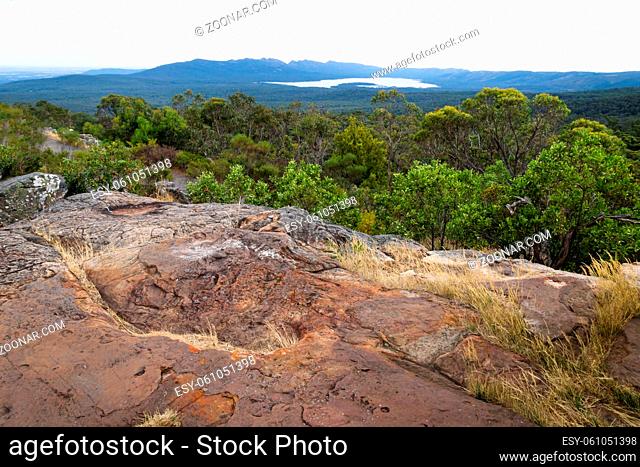 View into the valley and to a lake with red rocks in front at Reeds Lookout, Grampians, Victoria, Australia