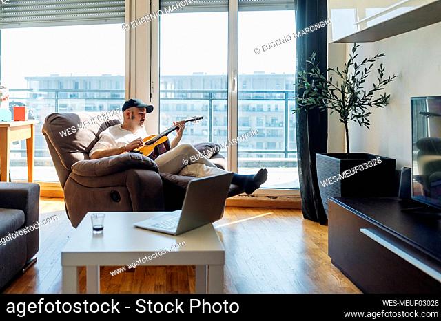 Man playing guitar while sitting on reclining chair at home