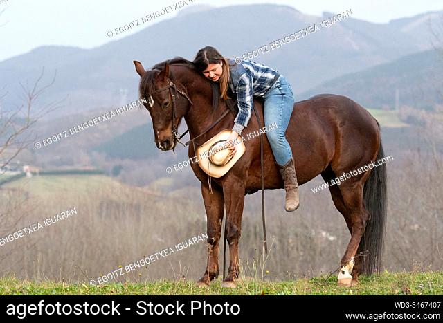 A young cowgirl lying on her horse without saddle with a hat in the hand