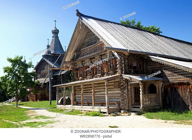 Ancient wooden church and wooden log hut on a forest glade. Russia