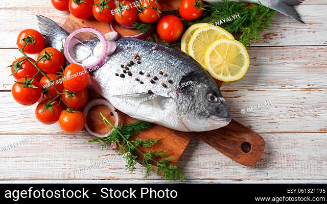 Raw fresh uncooked dorado or sea bream fish with lemon, herbs, cherry tomatoes and spices on black background