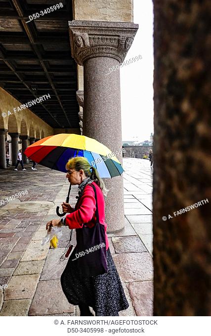 Stockholm, Sweden A woman walks by at City Hall or Stadshuset with a bright umbrella