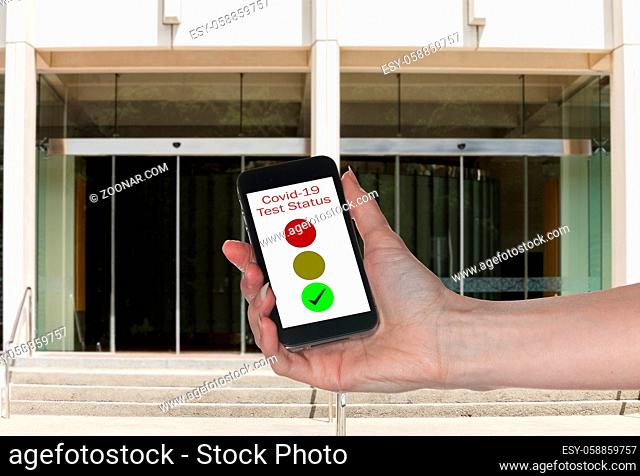 Mockup of entrance to office with hand holding smartphone app showing immunity to coronavirus