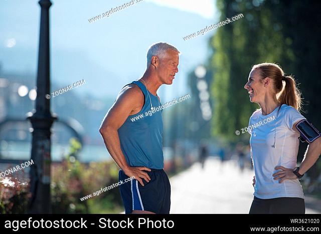jogging couple check music playlist on phone and plan route before morning running workout with sunrise in the city and sun flare in background