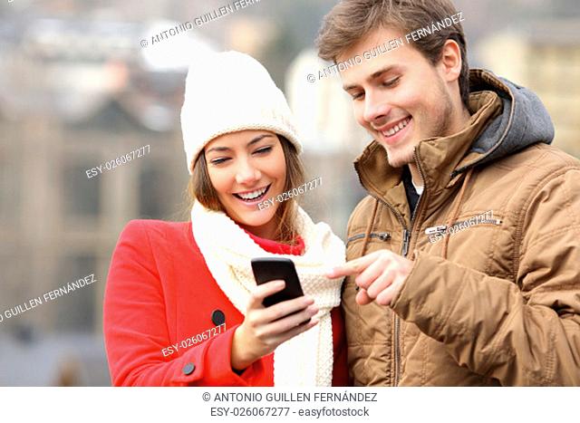 Happy couple consulting a smart phone in winter in the street