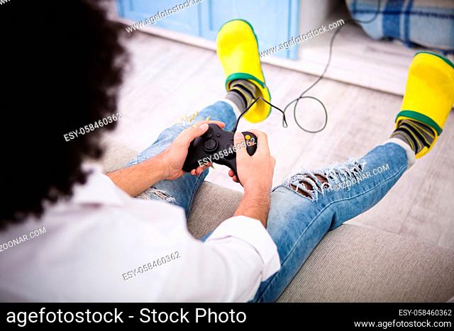 Hipster man sitting on sofa and playing computer games in front of television of laptop computer. Happy man in yellow crocks enjoying free time