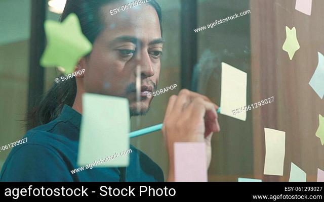 Businessman sticking adhesive notes on glass wall in creative in office, The man working write work with stickers reminder on paper on whidows