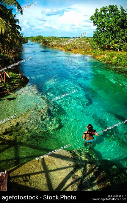 Woman swimming in sunny seven colored lagoon surrounded by tropical plants vertical in Bacalar, Quintana Roo, Mexico