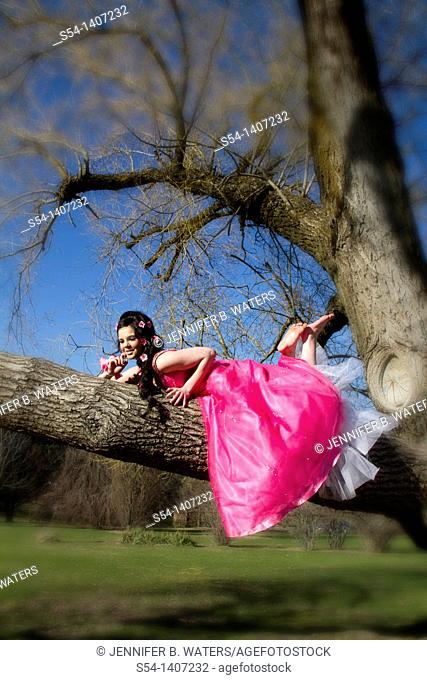 A young woman in a pink dress, laying in a tree