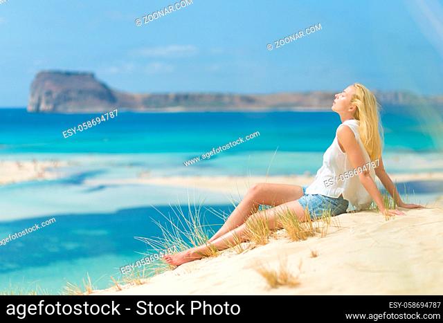 Relaxed woman enjoying sun, freedom and life an a beautiful sandy beach of Balos in Greece. Young lady feeling free, relaxed and happy