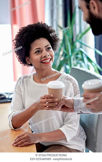 business, startup, people and drinks concept - happy african woman taking coffee cup from man in office