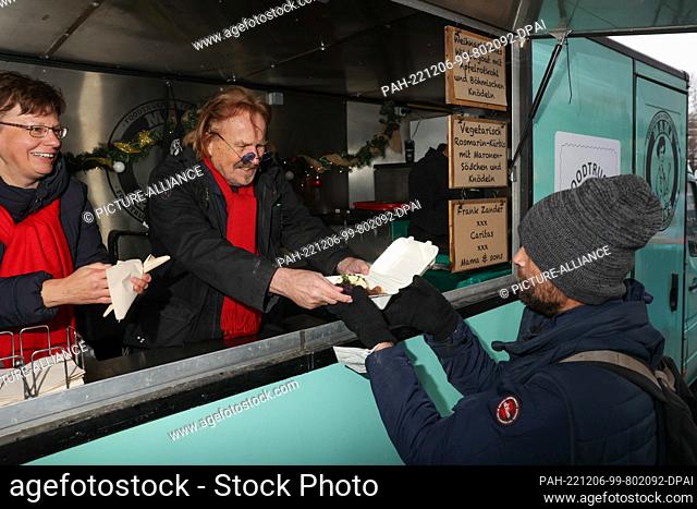 06 December 2022, Berlin: Frank Zander (m.) and Ulrike Kostka (l) from Caritas hand out a hot meal to someone in need at the press conference for the start of...