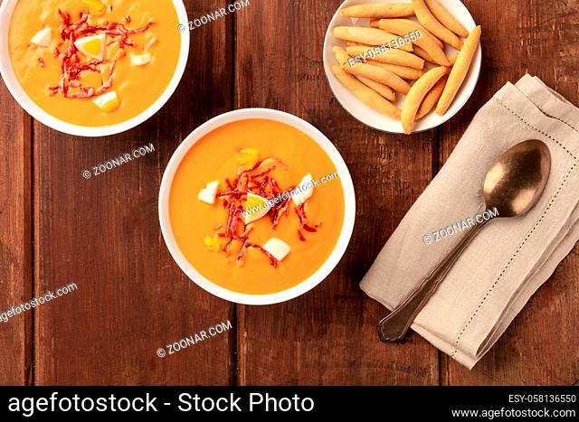 Salmorejo, Spanish cold tomato soup, shot from the top on a dark rustic wooden background with picos, typical breadsticks