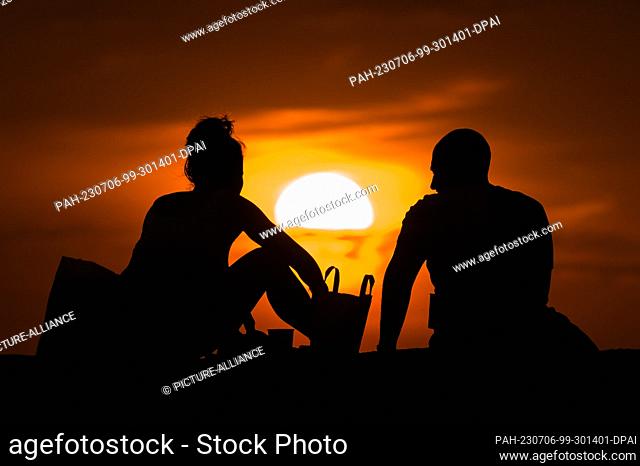 SYMBOL - 05 July 2023, Serbia, Belgrad: A woman and a man are sitting on a wall at Kalemegdan Park at sunset. Thereby they can be seen as a silhouette