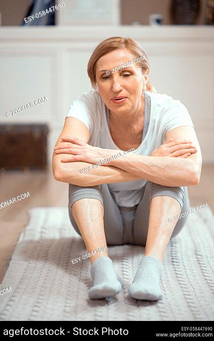 Exhausted Mature Woman Catches Her Breath After Actively Practicing Yoga. Charming Woman Breathes While Sitting On A Mat Resting