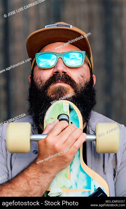 Portrait of bearded man with skateboard wearing mirrored sunglasses