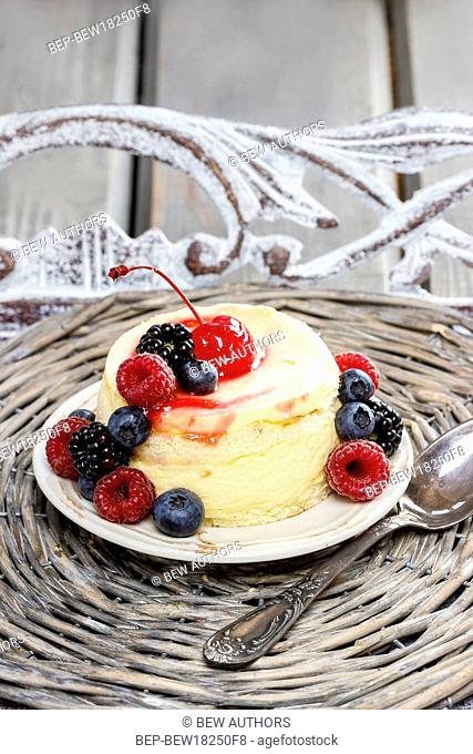 Round vanilla cake decorated with fresh fruits: cherries, blueberries, blackberries and raspberries. Yummy dessert on wicker tray