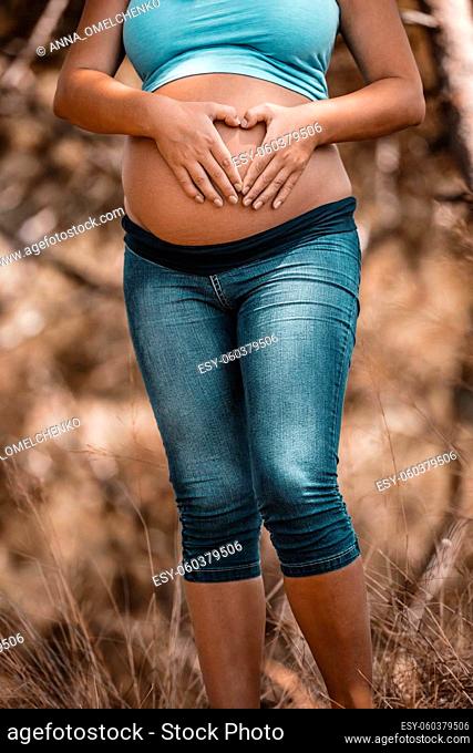 Tummy of a Pregnant Woman Making Heart Shape by her Hands on it. Healthy Activities Outside. Spending Warm Autumn Day in the Park. New Life Concept